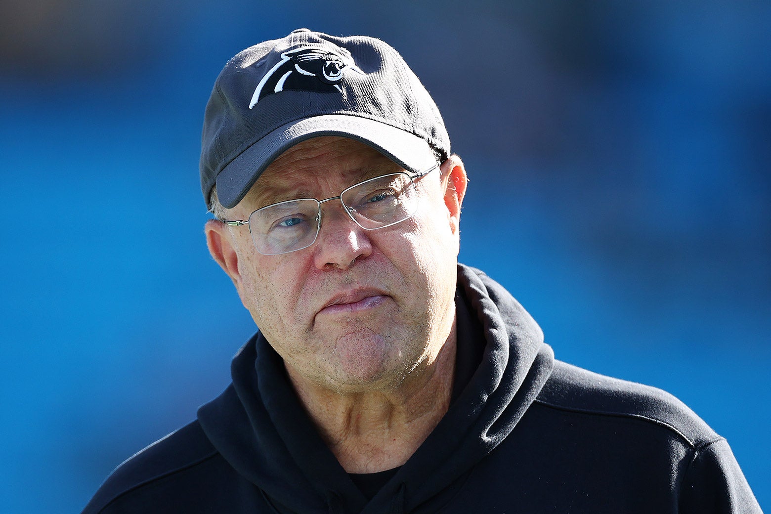 David Tepper in a Panthers hat and hoodie, frowning