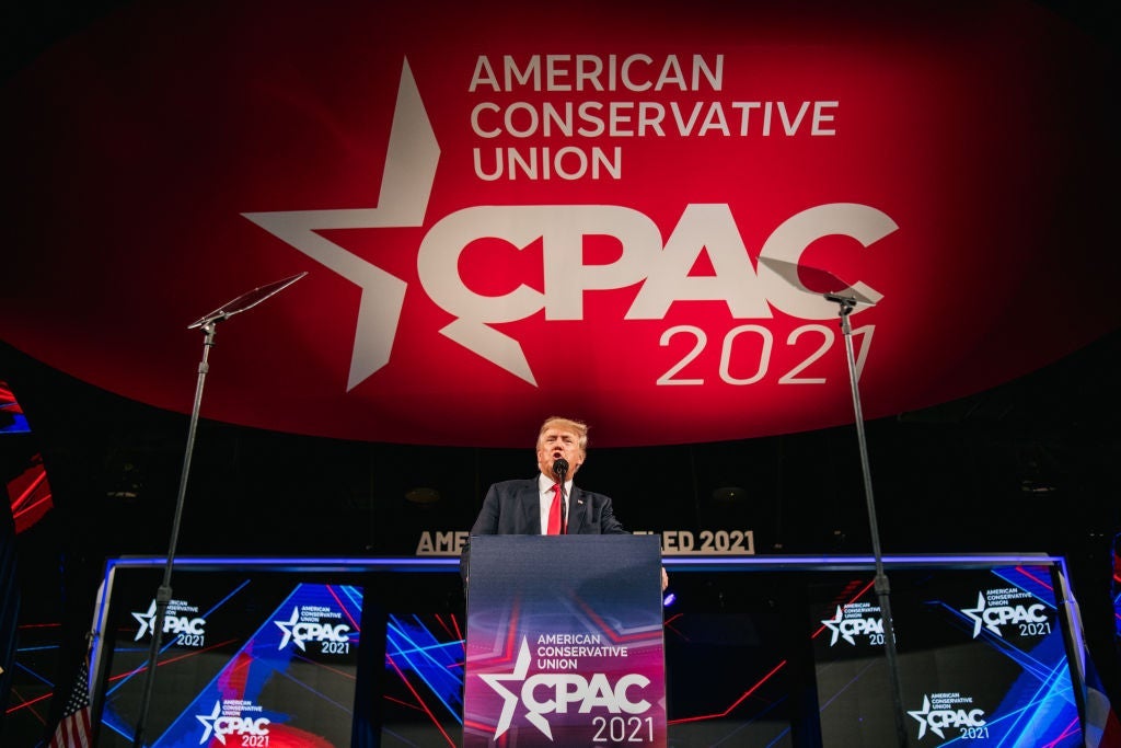 Trump speaks at a lectern in front of a backdrop of CPAC logos.