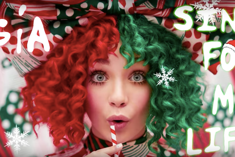 Maddie Ziegler wears a red and green wig and stares directly into the camera, lips puckered.