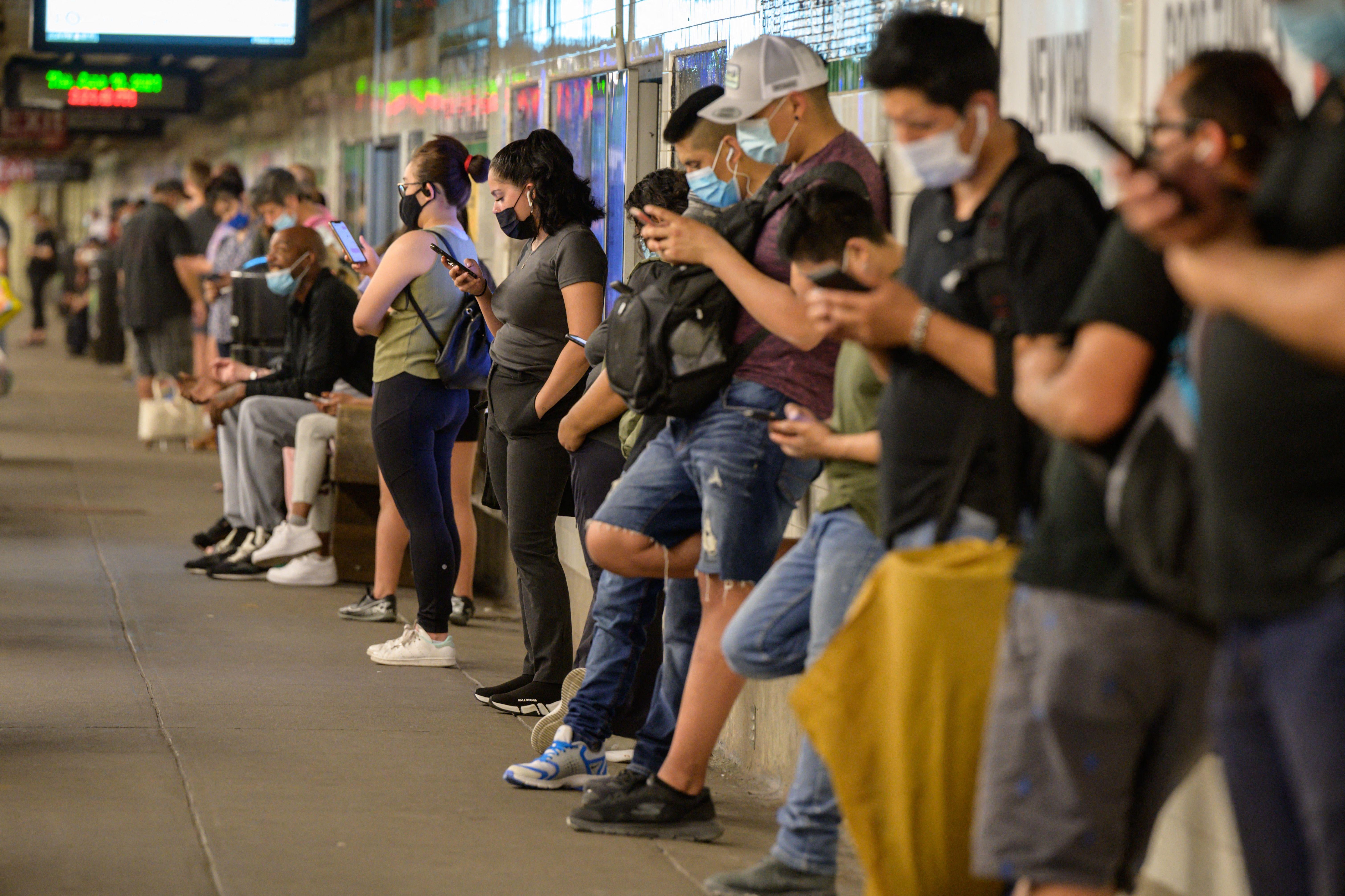 Commuters look at their mobile phones as they wait for a subway train in New York.