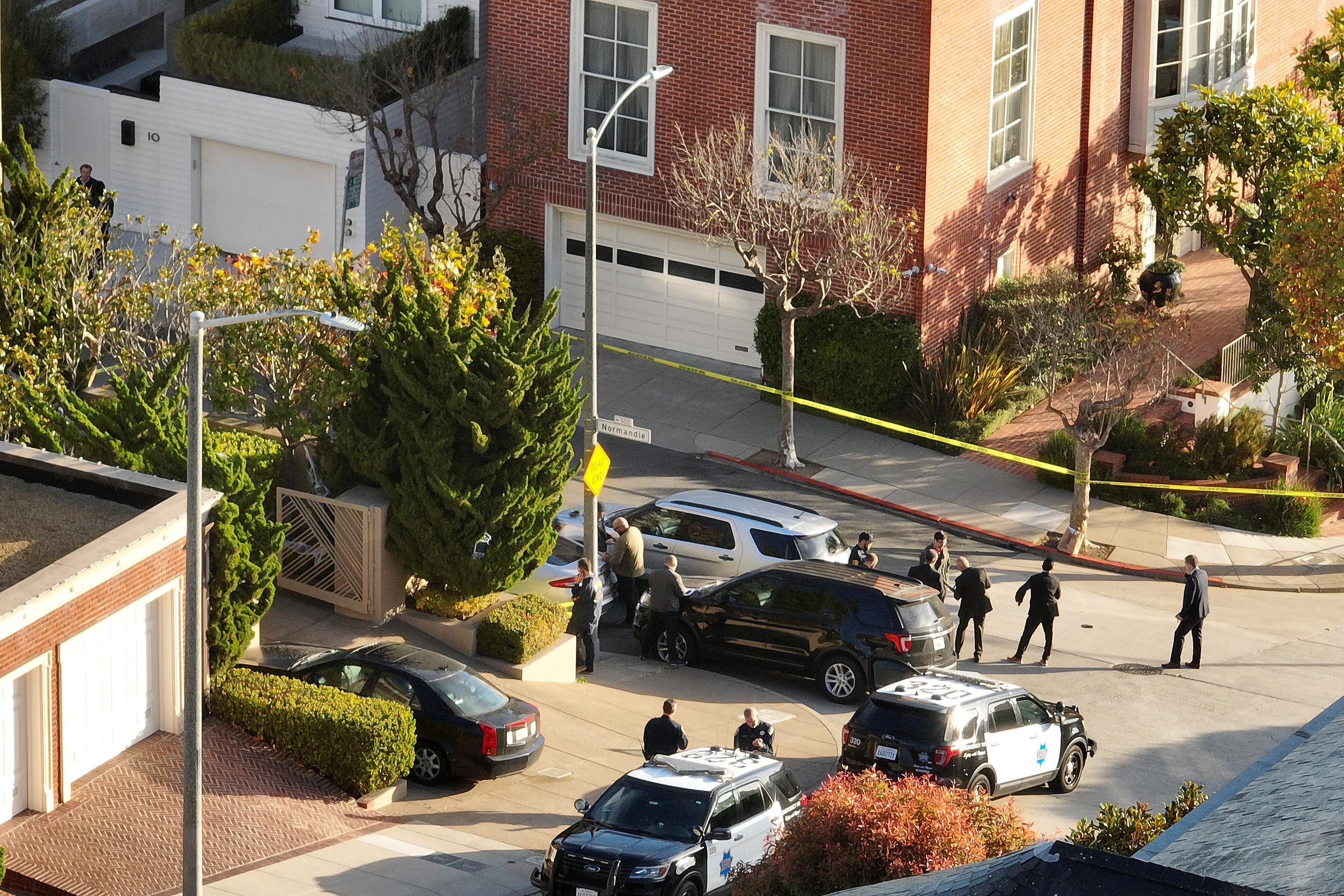 Yellow tape closes off a quiet-looking road in an aerial view. Four police vehicles are stationed outside the tape.
