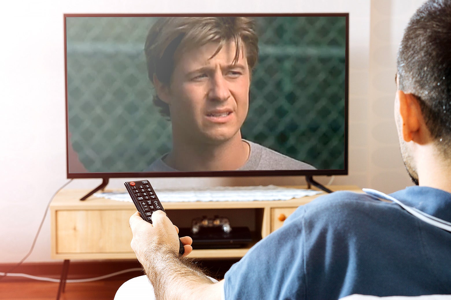 A man holding a remote watching The OC on his large television.