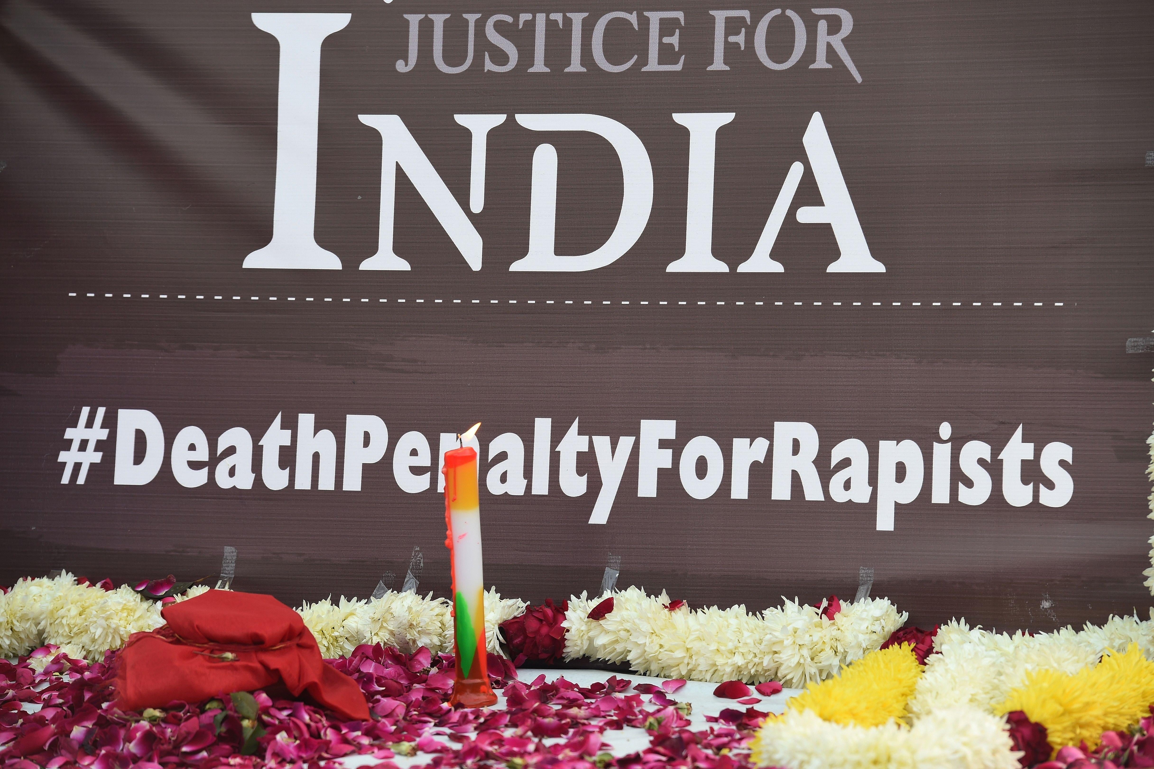 A candle lit by demonstrators is seen in front of a banner reading "Justice for India" and "#DeathPenaltyForRapists."