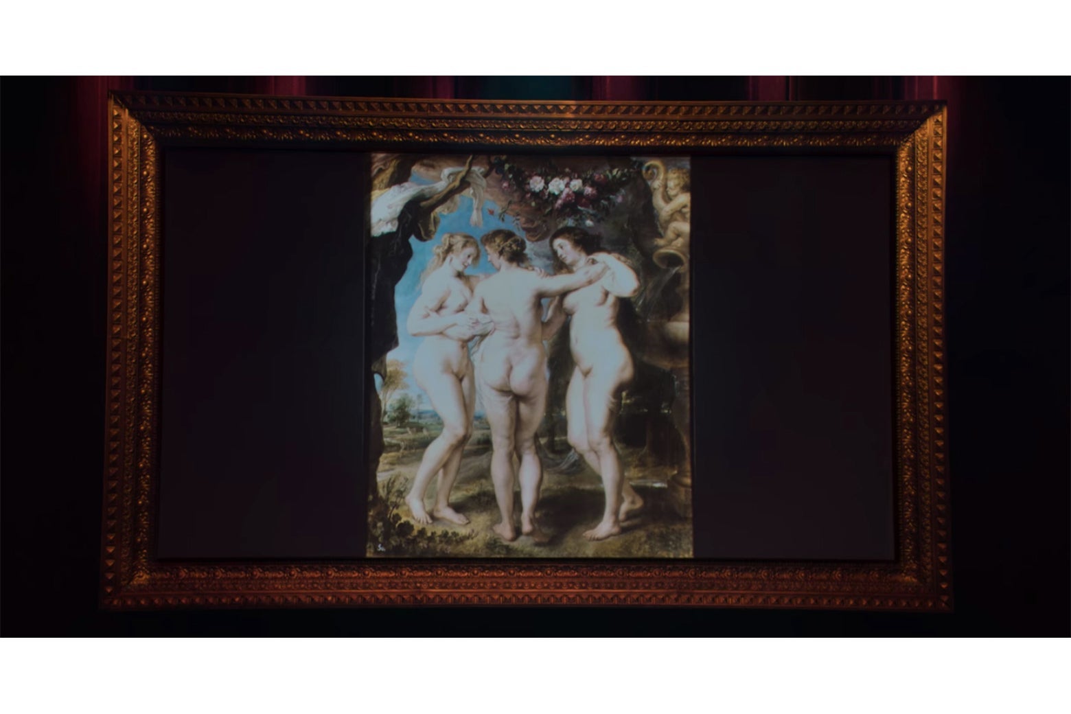 A projection screen showing Rubens' painting of the Three Graces, wrapped in an ornate frame.
