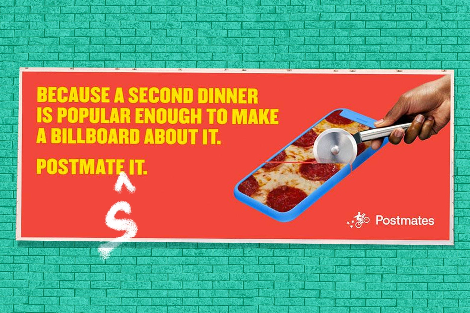 On a brick wall, a Postmates billboard reading "Because a second dinner is popular enough to make a billboard about it. Postmate it," with an S and a caret graffitied in under "Postmate."