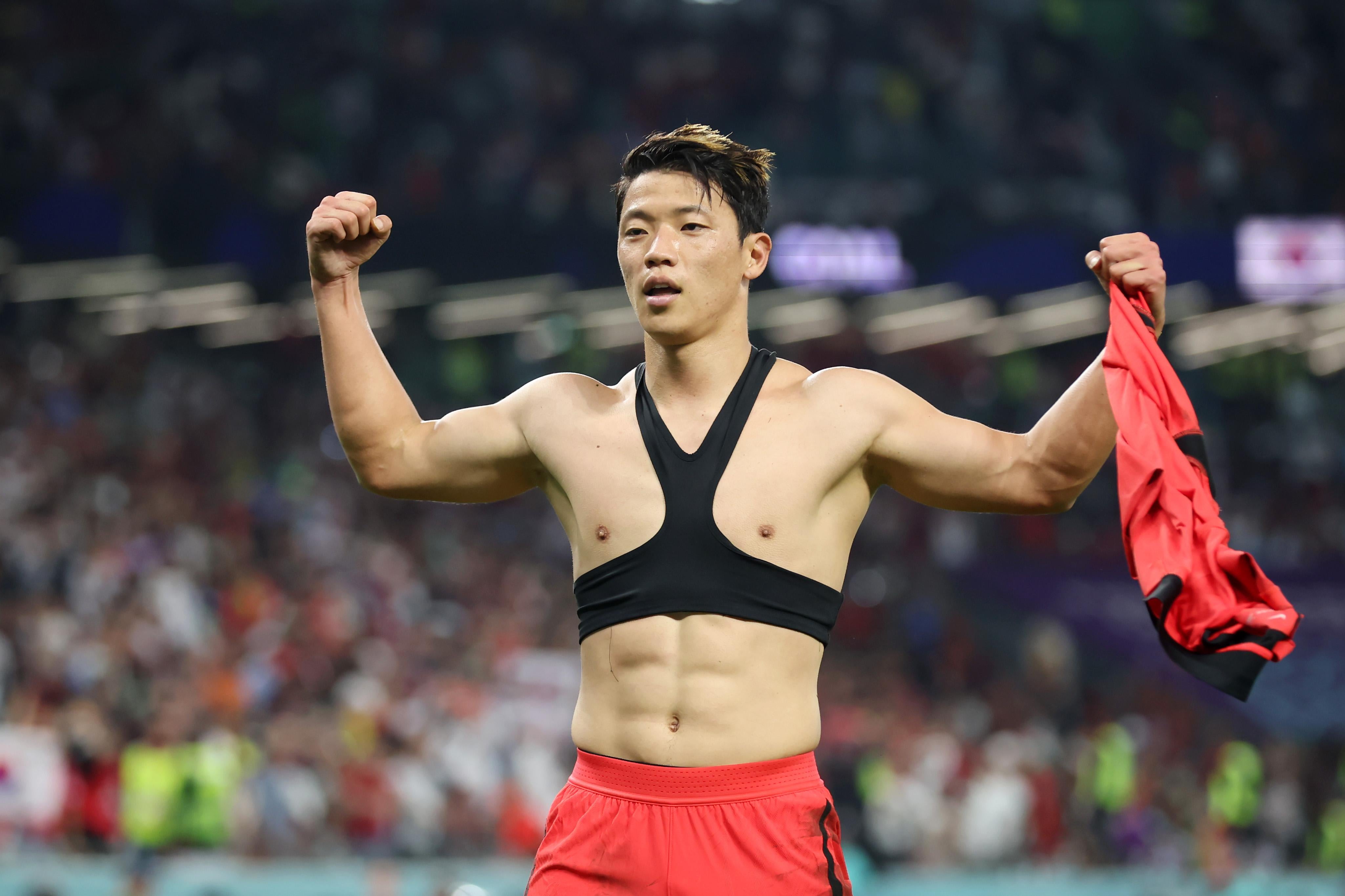 A Korean soccer player poses with his shirt off after scoring a crucial goal, wearing what appears to be some kind of harness or sports bra.