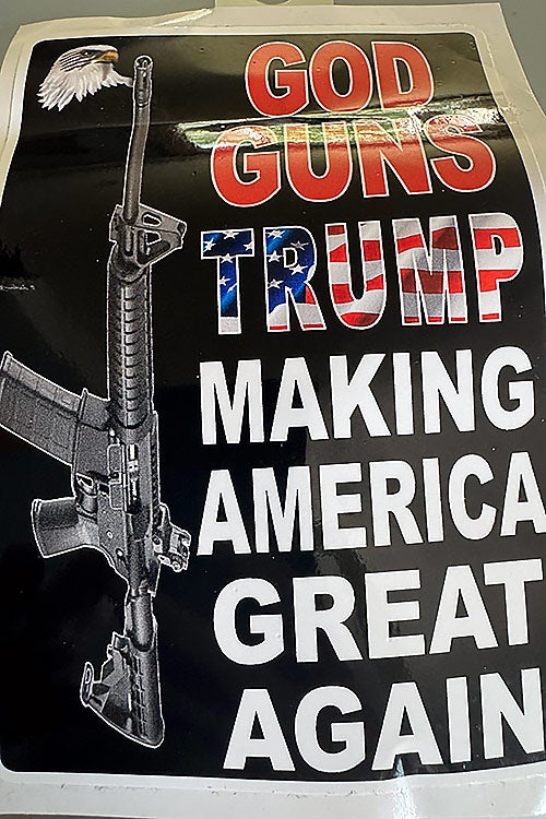 A sticker with a black rifle positioned vertically alongside a small bald eagle. Prominent text in bold red, white, and American flag-patterned font reads "GOD GUNS TRUMP MAKING AMERICA GREAT AGAIN" against a black background.