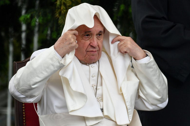 Pope Francis grabs his cape, which drapes over his head.