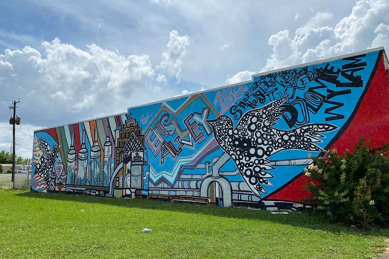 A mulitcolored mural on a building wall says "Ensley alive" and features flying birds.