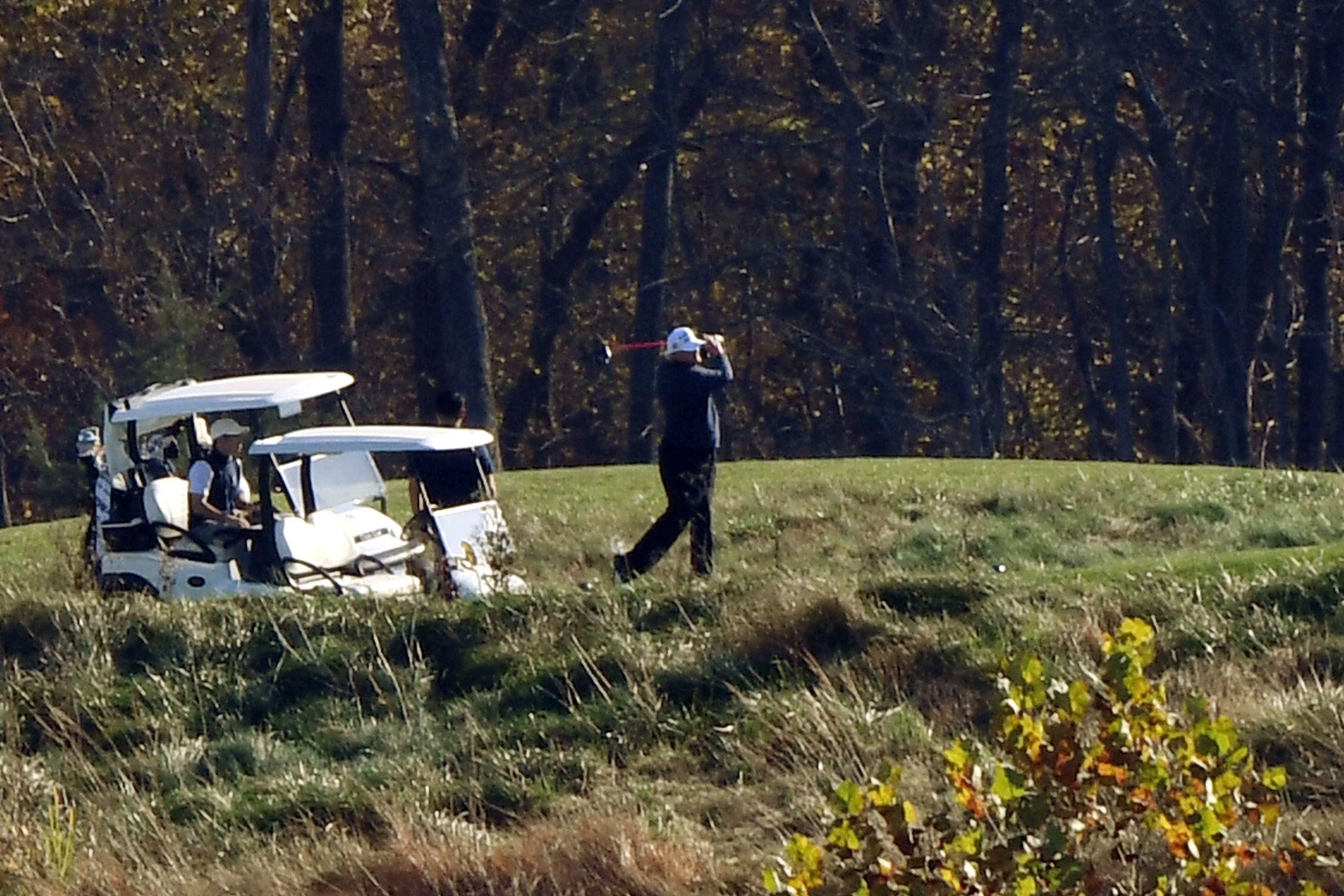 Trump plays golf while standing next to a golf cart, looking like a loser.
