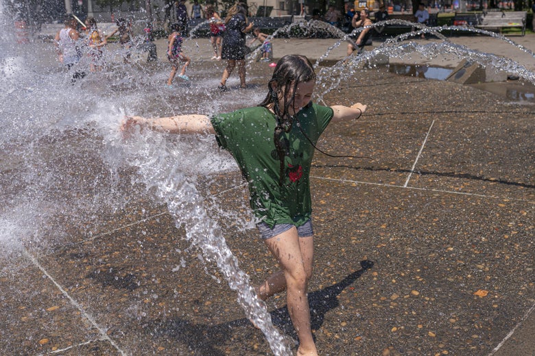 A child with outstretched arms stands in a fountain's stream of water. 