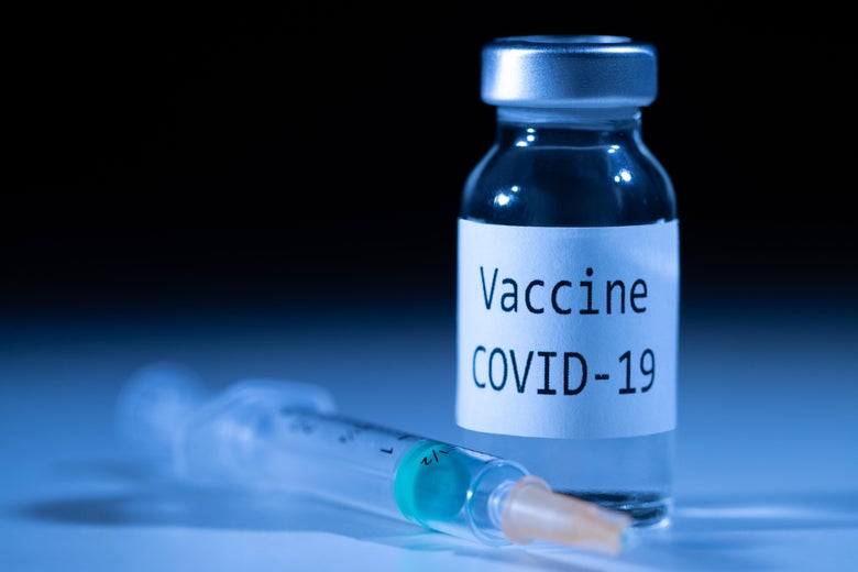 A syringe sits next to a vial labeled "Vaccine COVID-19."