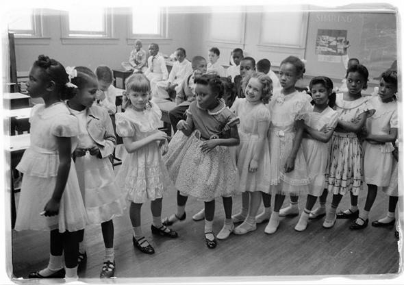 A line of African American and white school girls standing in a classroom while boys sit behind them, May 1955, Barnard School, Washington, D.C.
