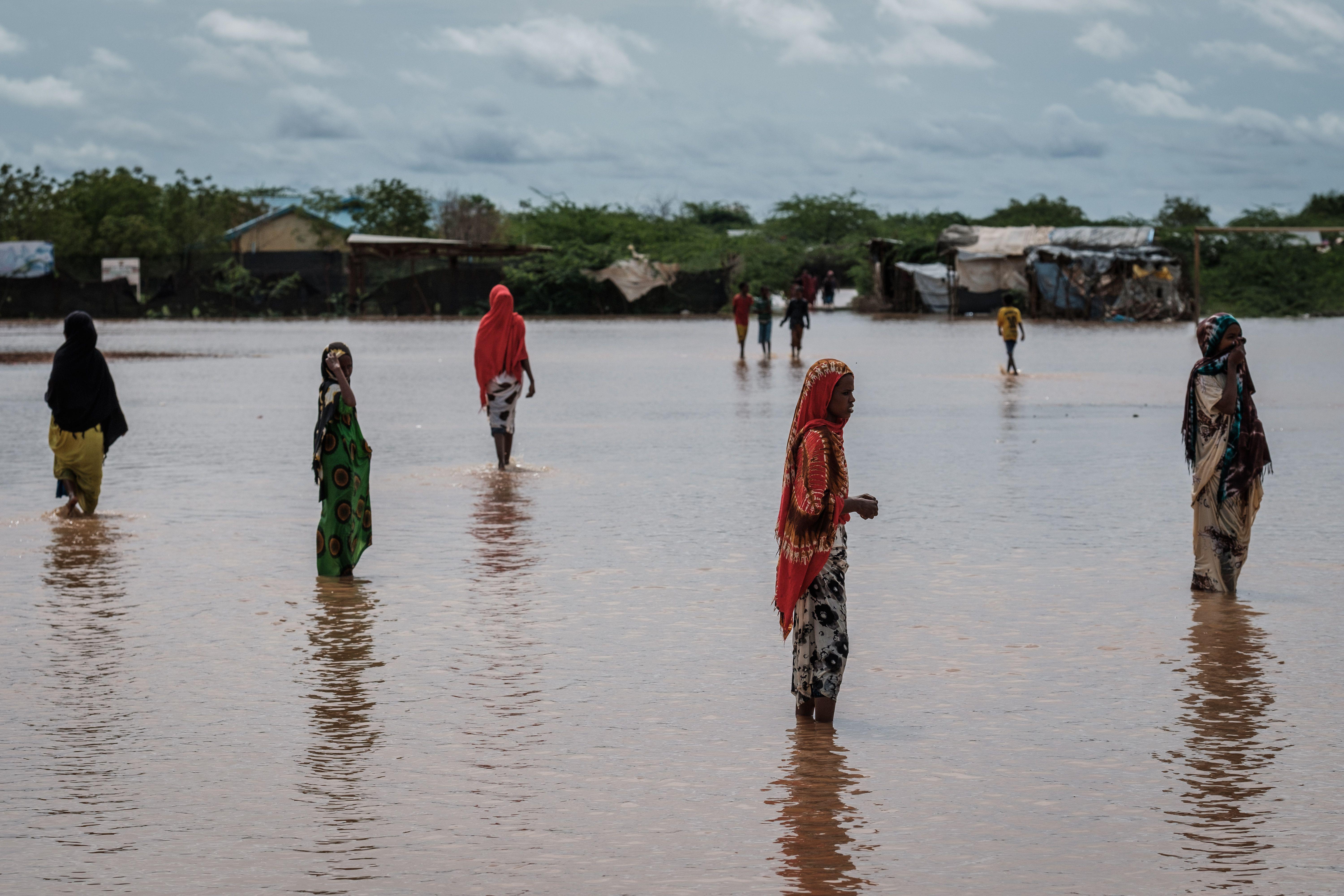 Women walking in ankle deep water outside a refugee camp.