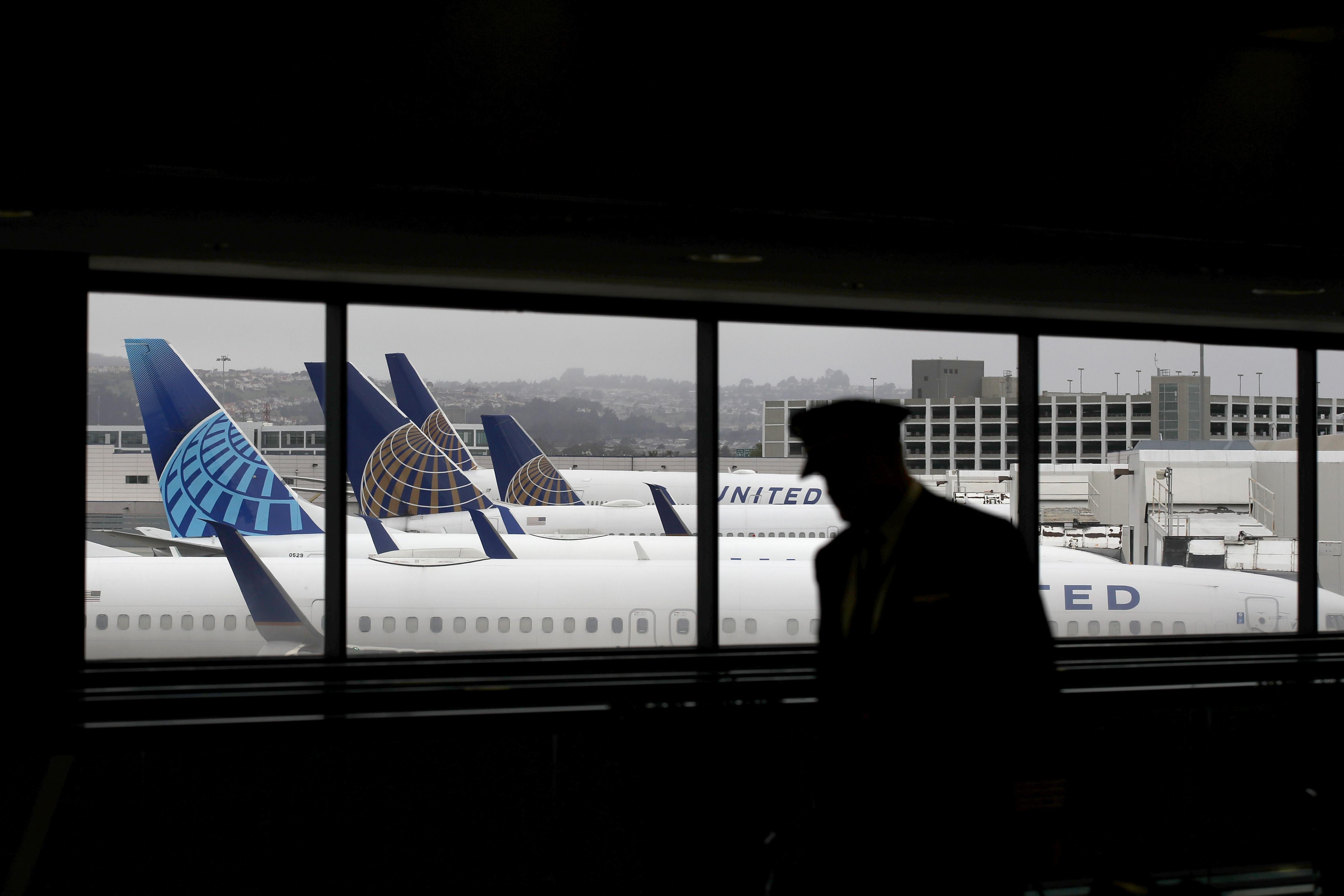 A pilot walks by a window, through which multiple parked United Airlines planes are visible.