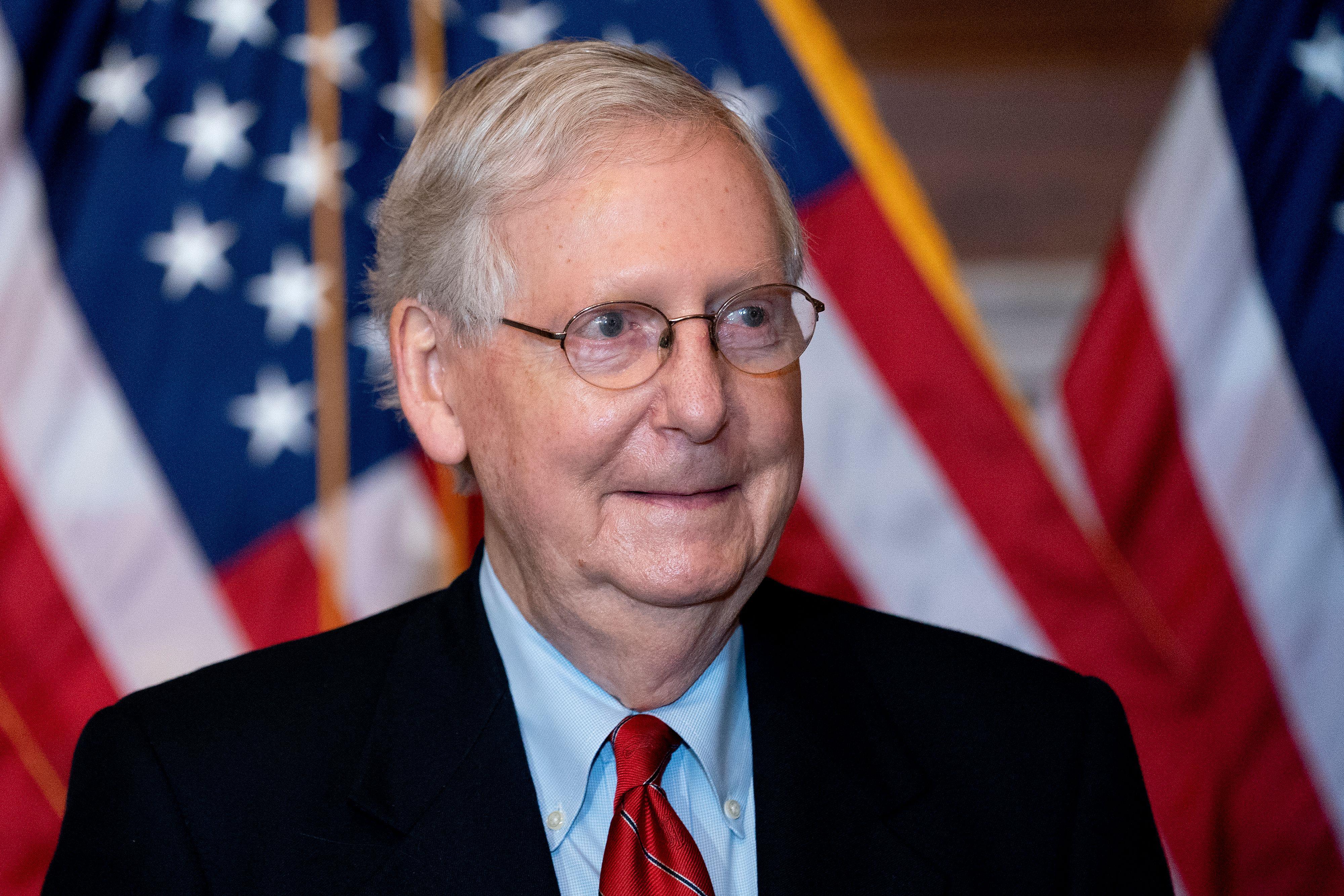 Mitch McConnell makes a closed-mouth smile in front of U.S. flags.