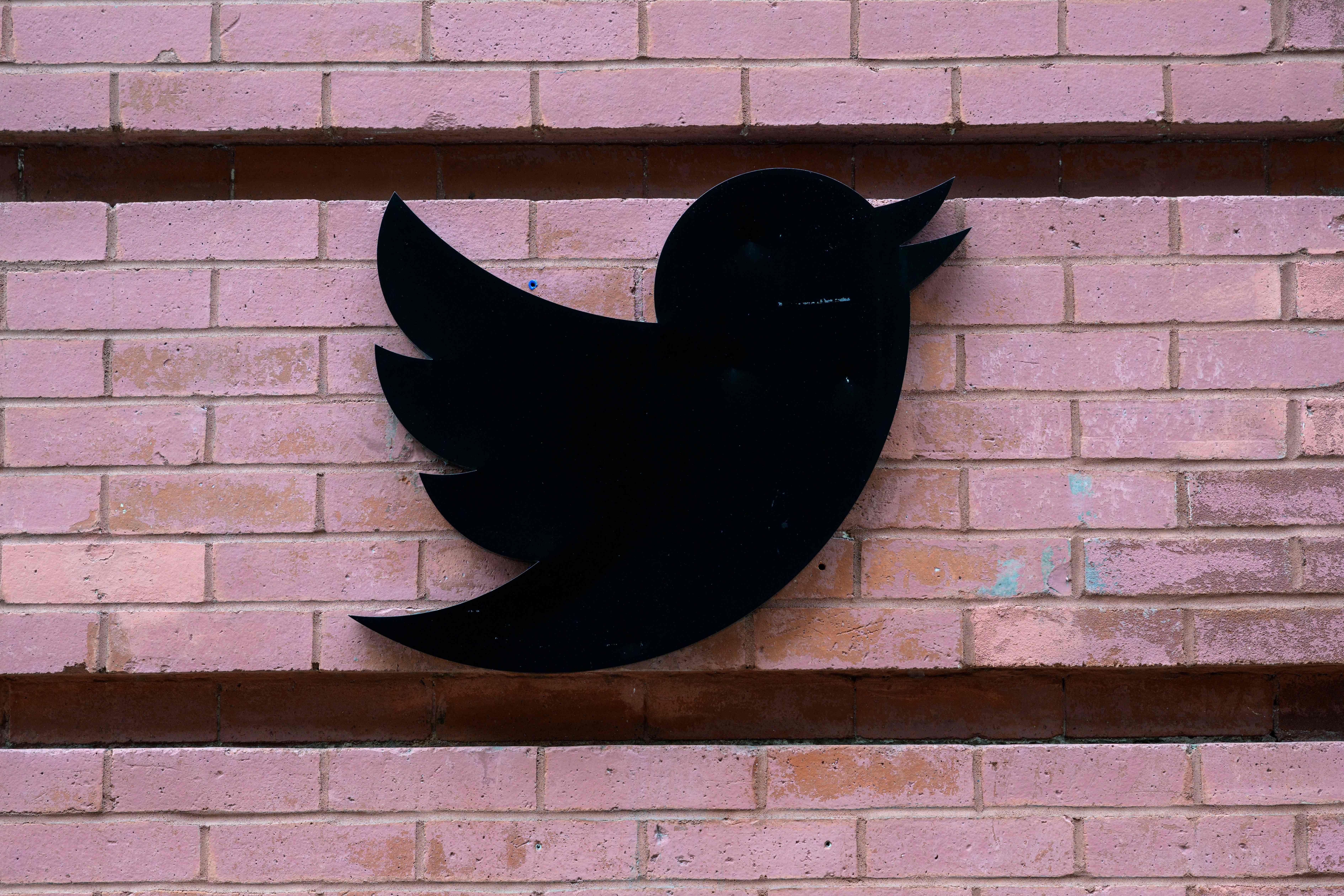 A black Twitter logo against a brick wall.