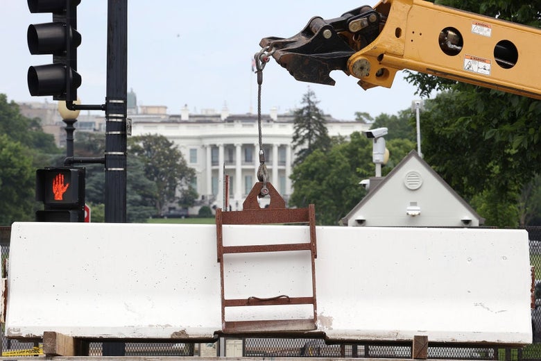 A crane lowers a heavy white barrier into place on a street facing the White House.