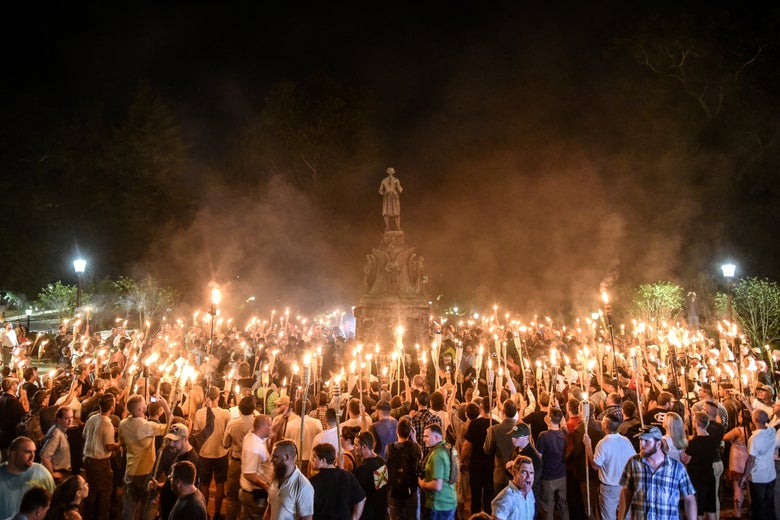 A crowd of people holding tiki torches surrounding a Confederate monument at night