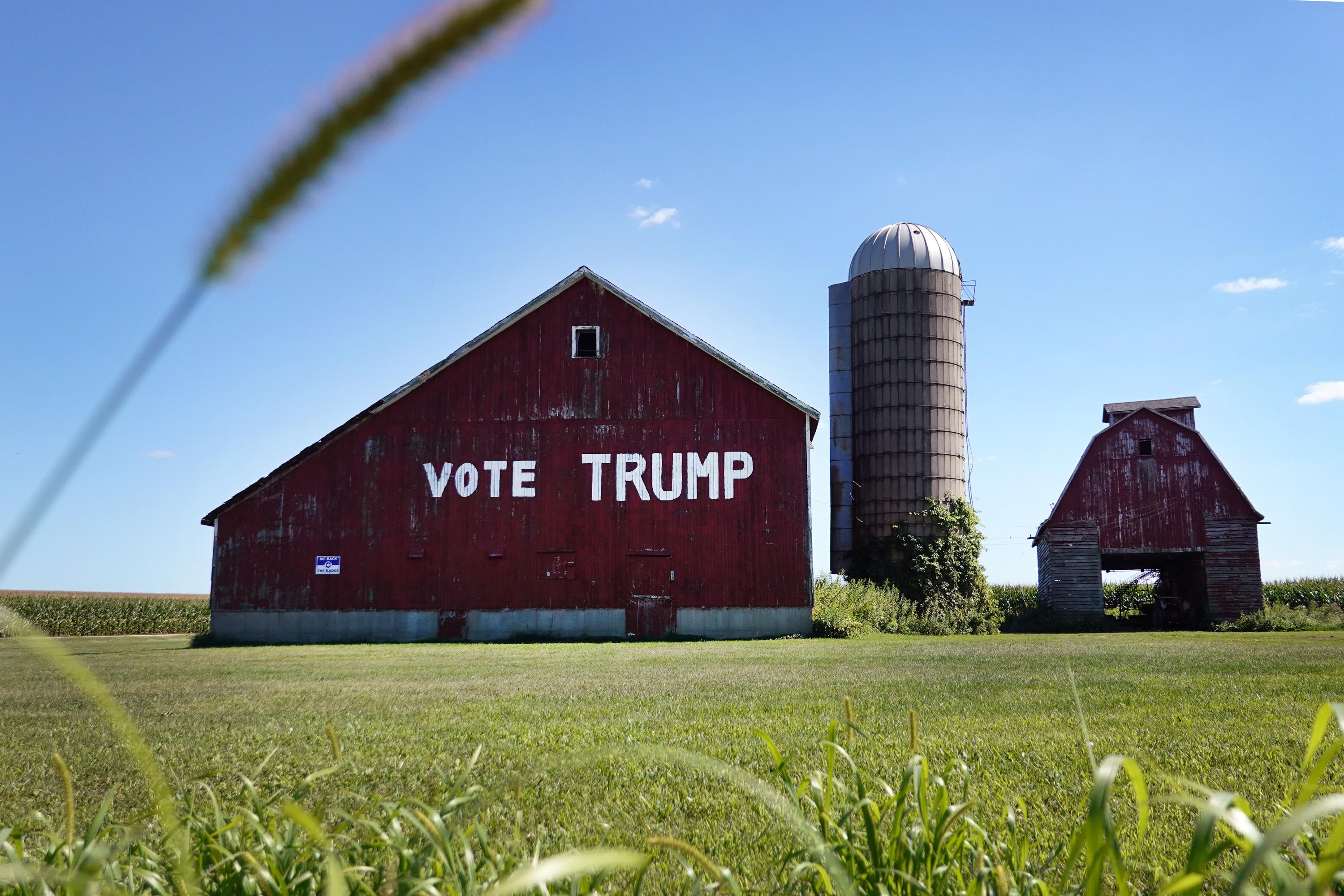 A red barn with "Vote Trump" painted on it near Clinton, Wisconsin. The barn stands next to a silo amid green grass on a sunny day.