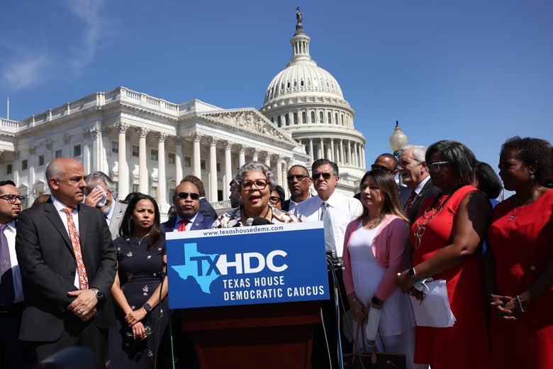 Senfronia Thompson speaks at a podium bearing a placard that says "TXHDC Texas House Democratic Caucus." Her fellow legislators stand around her and the U.S. Capitol dome looms in the distance on a clear day.