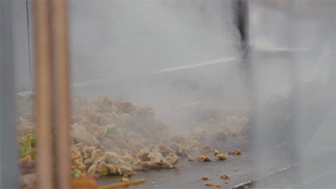 A vendor slides food around a grill.