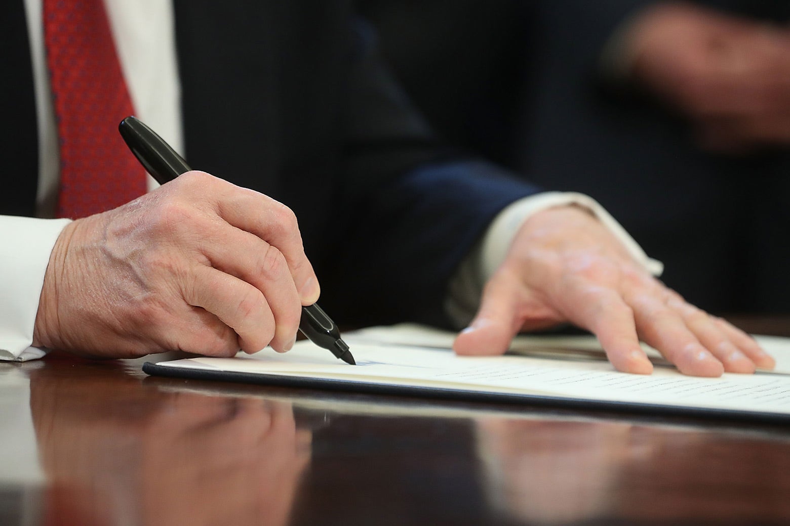Trump signing a paper with a pen.