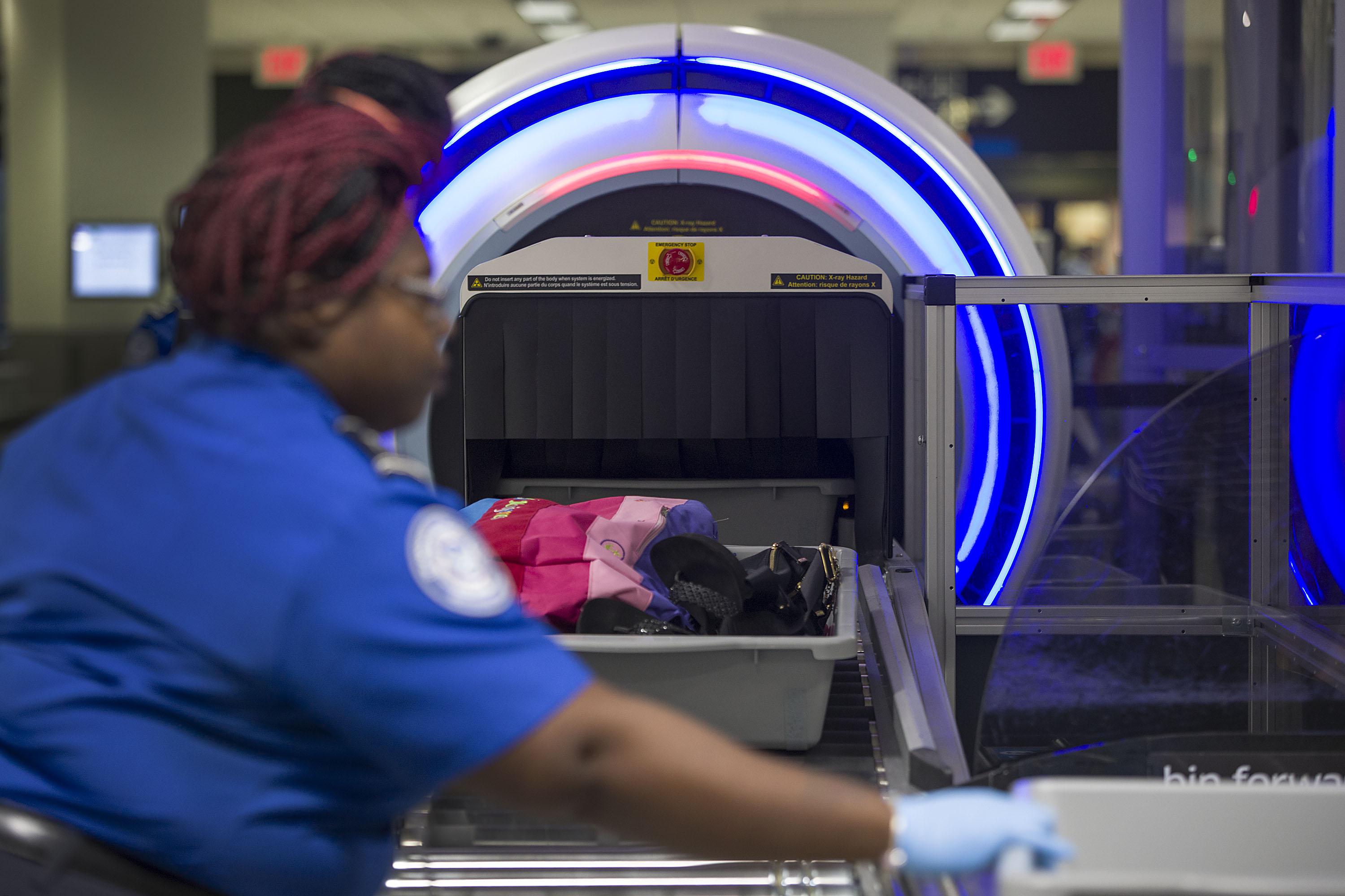 A TSA agent on the left sends luggage through a screener.