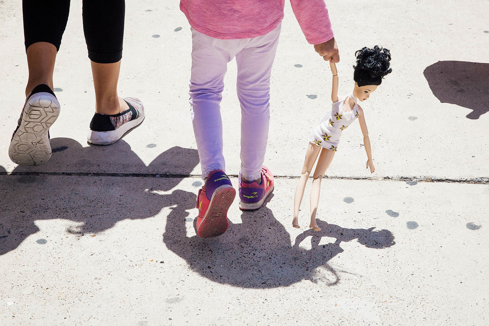 A 4-year-old Honduran girl carries a doll while walking with her immigrant mother.