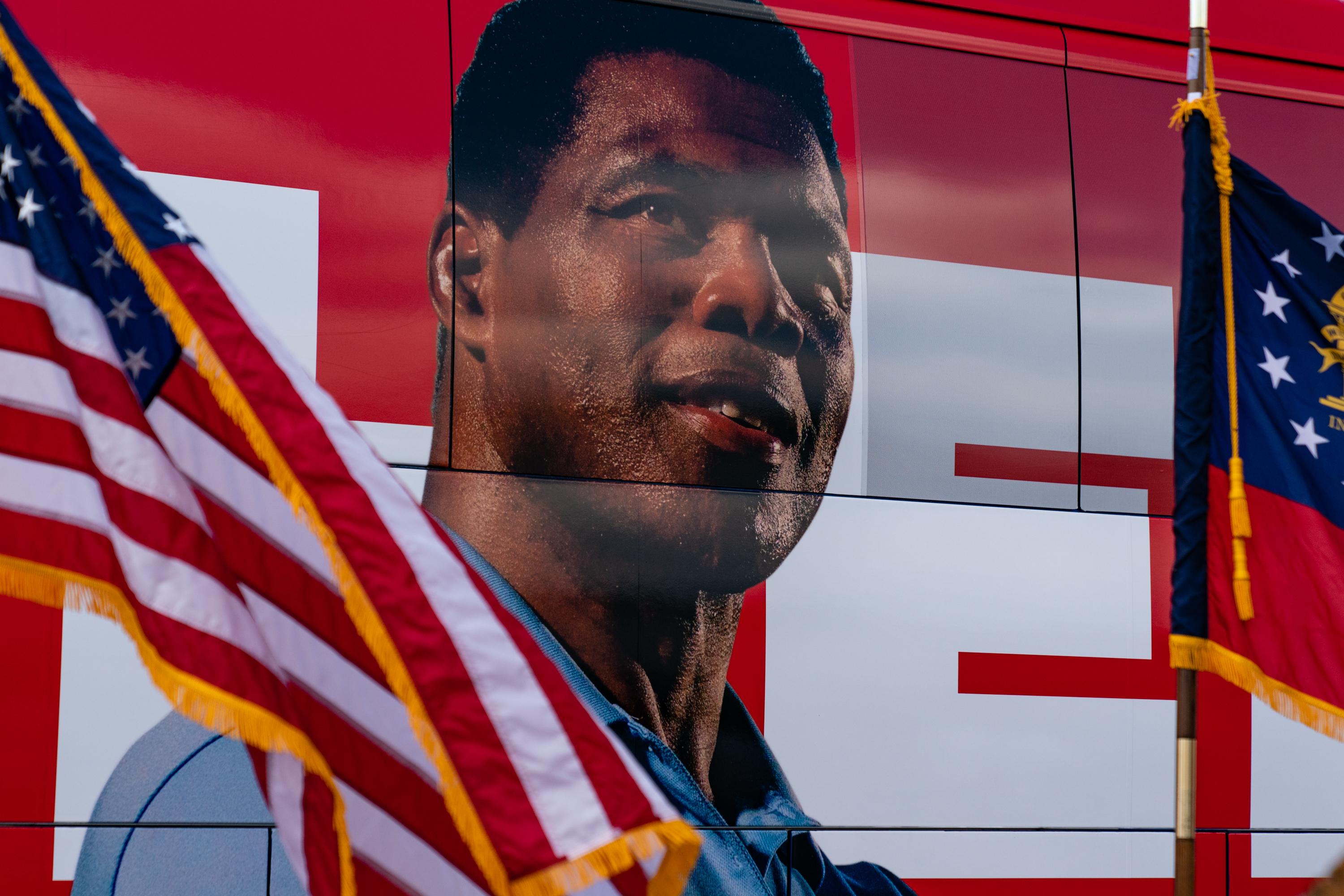 U.S. and Georgia state flags fly in front of the Herschel Walker campaign bus, which has a huge replication of his face displayed on one side.