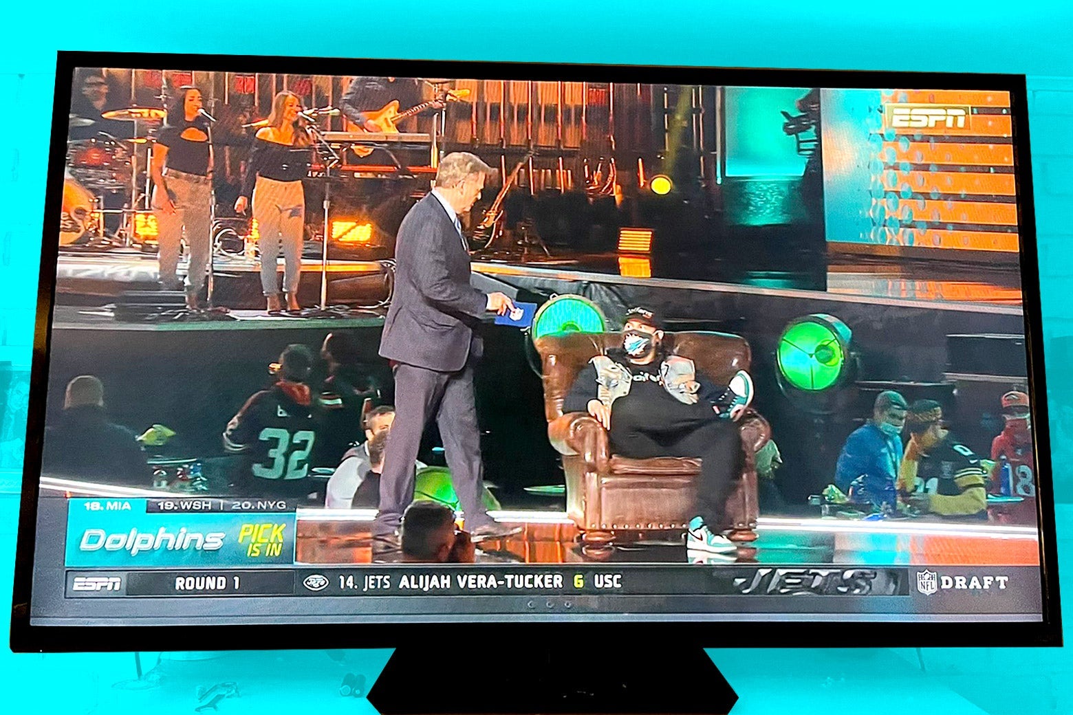 Goodell stands next to Smith, sitting in his chair, at the NFL Draft on flat-screen television
