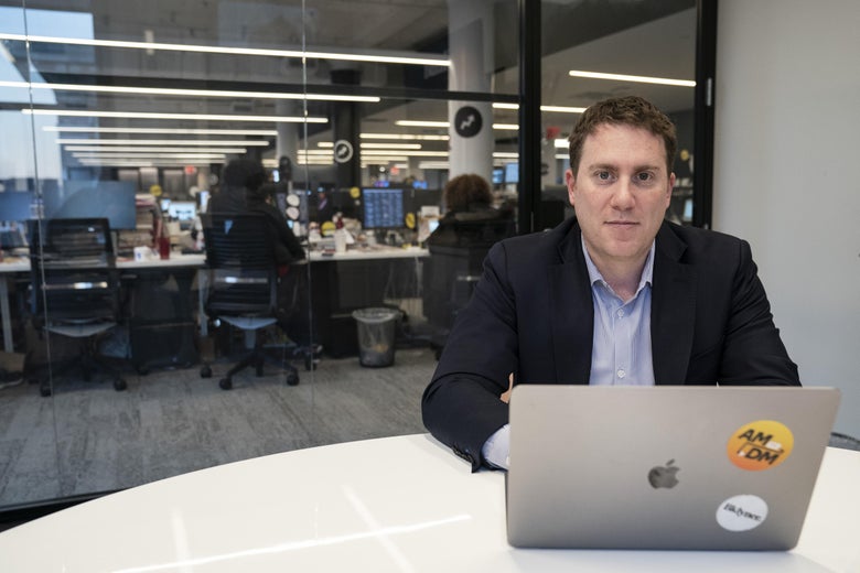 Ben Smith sits at a table with his laptop. In the background, an office environment with chairs and computers can be seen.