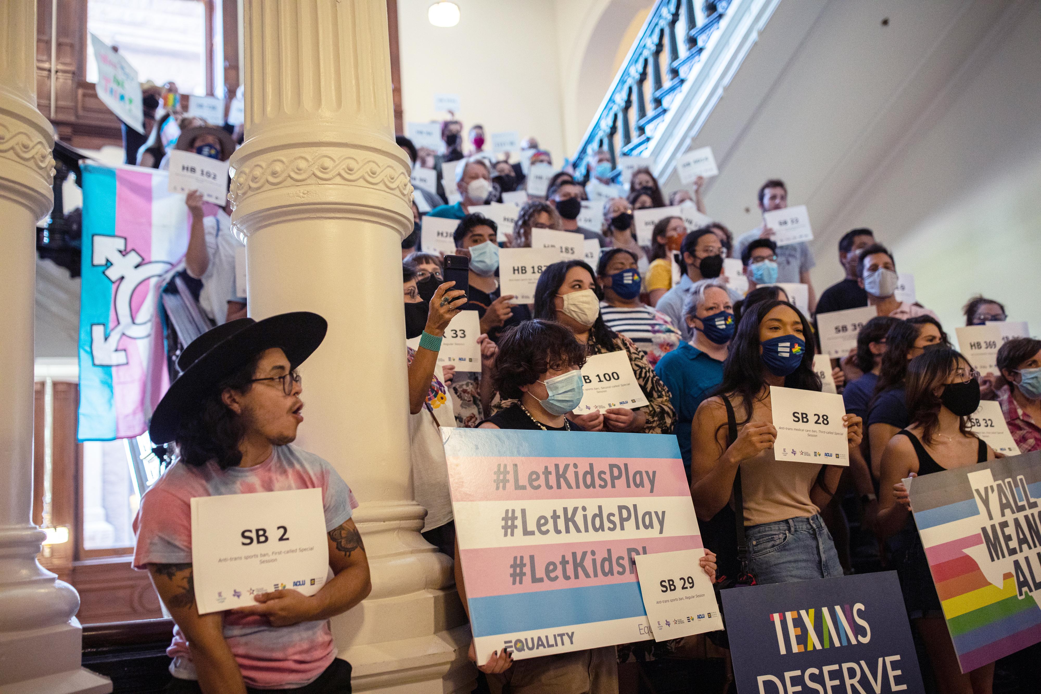 LGBTQ advocates stand on steps holding signs in support of LGBTQ rights.