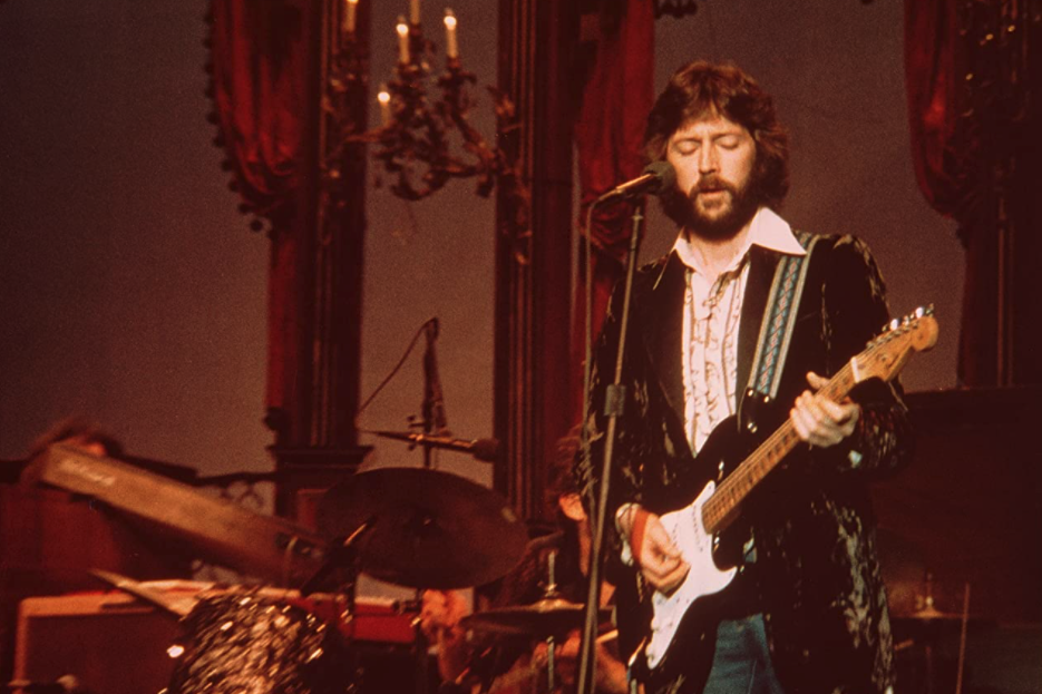 Eric Clapton stands on stage behind a microphone, holding a guitar