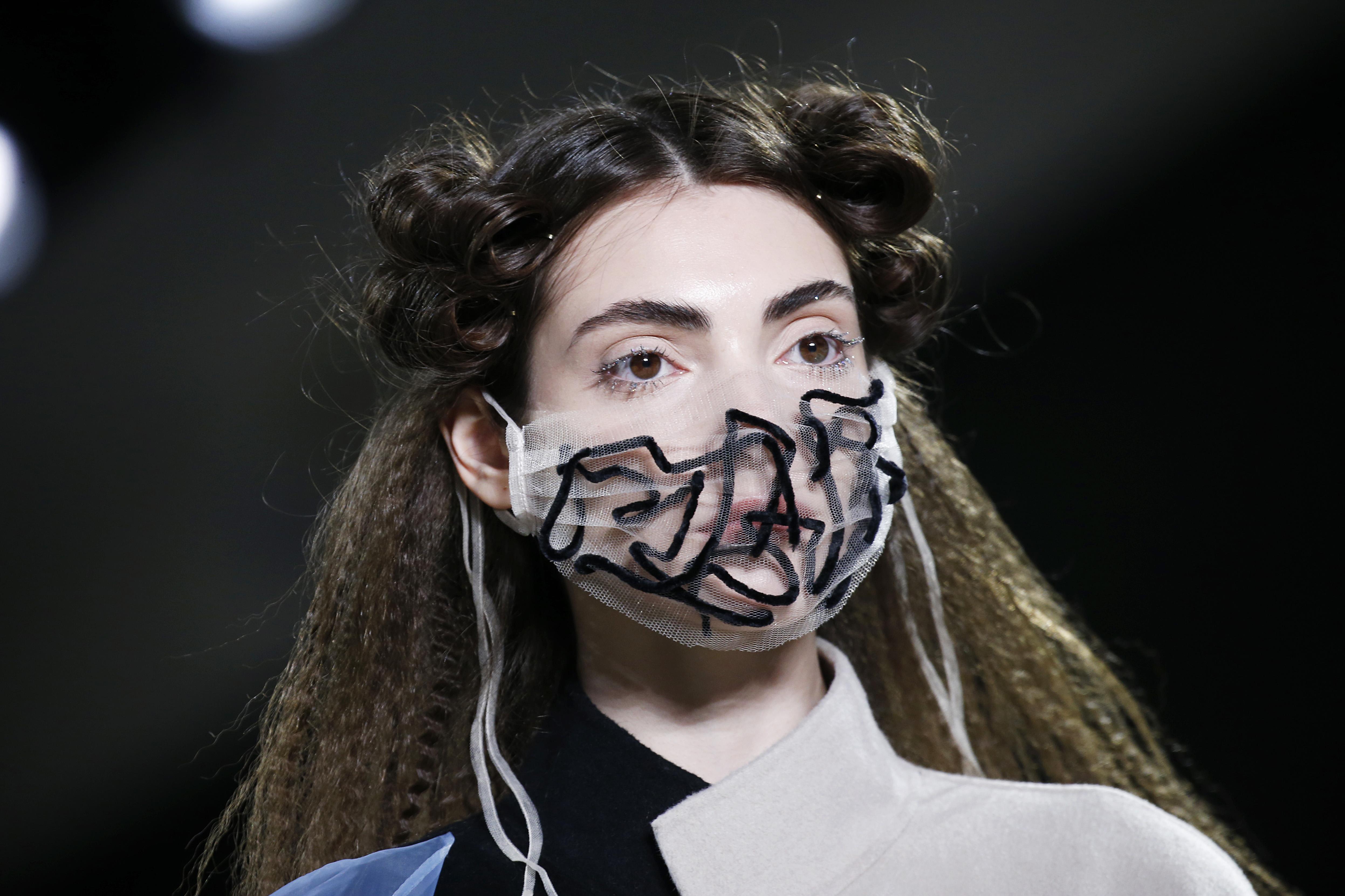 A model with crimped hair and a face mask made of white mesh.