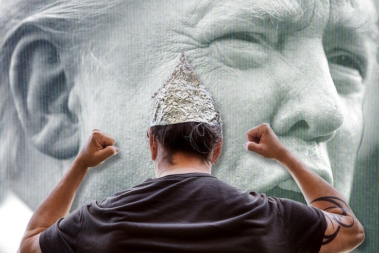 A man in a tinfoil hat pumps his fists in front of a projection of Trump's face.