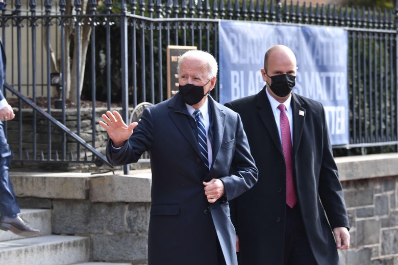 A masked Biden waves to crowds as he leaves church.