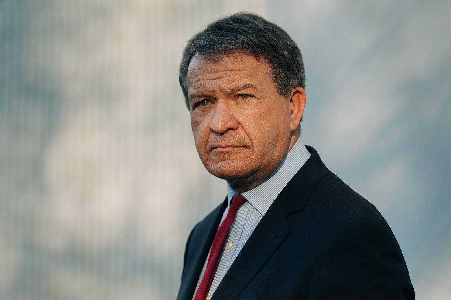 A white man with gray hair wears a red tie and a blue suit.