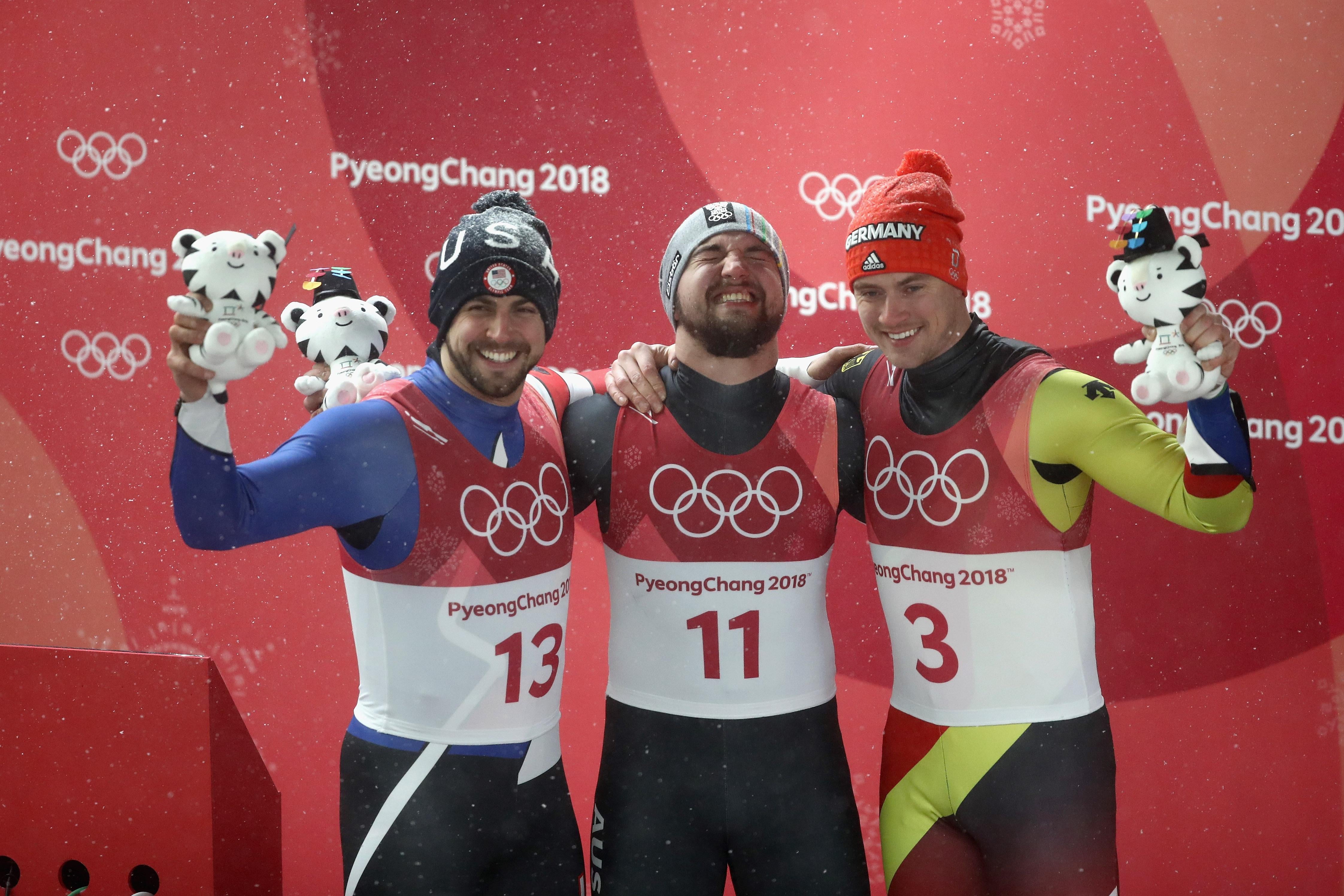 Chris Mazdzer (silver) of the United States, David Gleirscher (gold) of Austria, and Johannes Ludwig (bronze) of Germany celebrate at the flower ceremony.