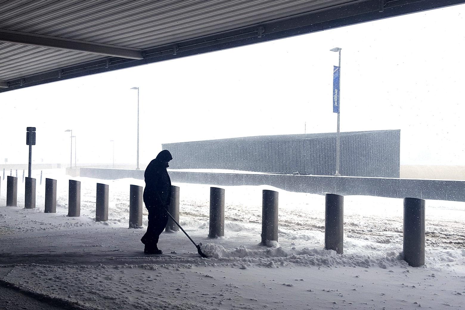 An airport employee shovels snow at the curb of the departures drop-off area.