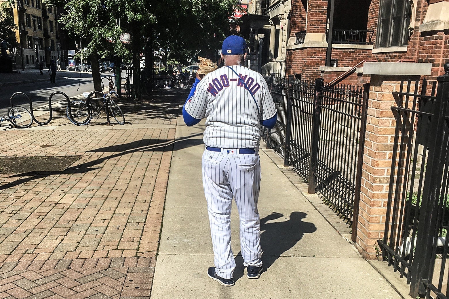 Man standing on a sidewalk, wearing a baseball uniform with the name WOO-WOO on the back