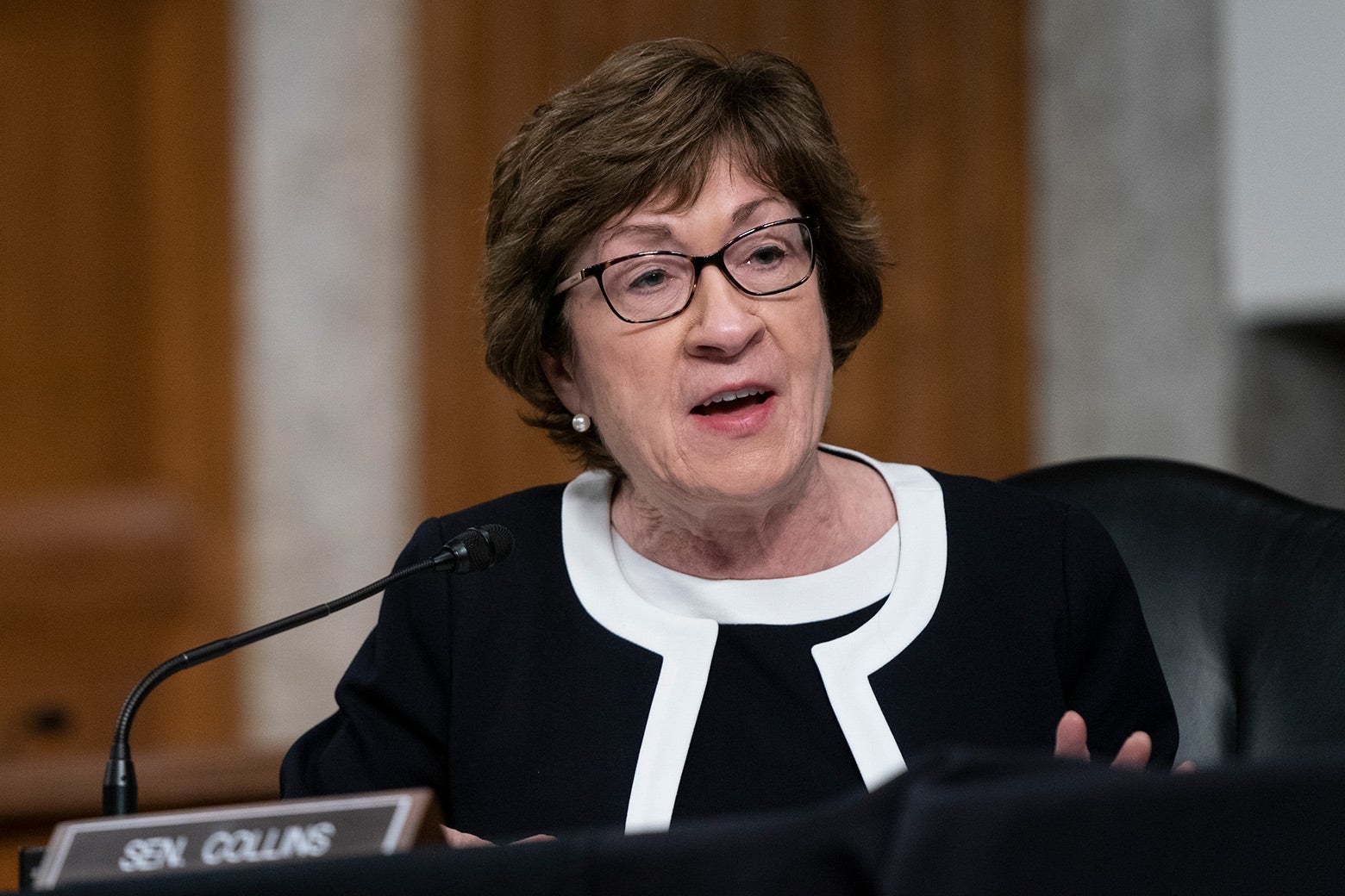 Susan Collins sits at a desk and speaks into a microphone.