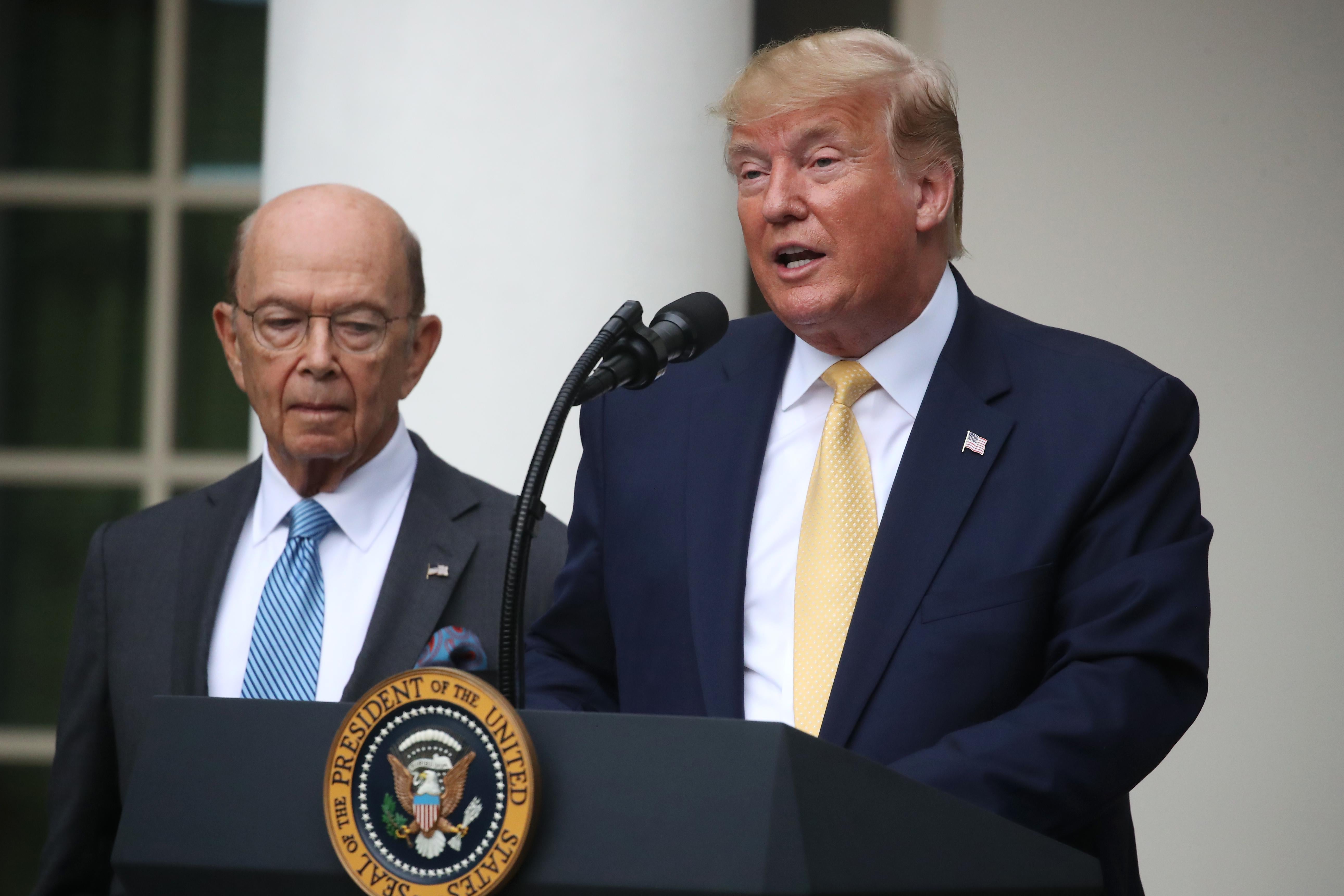 Trump speaks at a lectern while Wilbur Ross stands next to him.