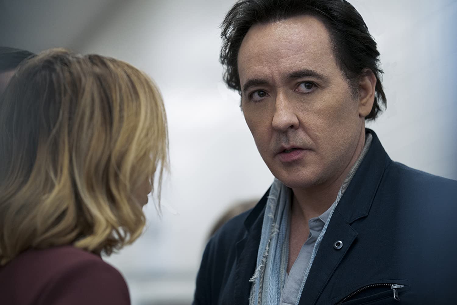 John Cusack is seen standing with a woman in a still from Amazon's Utopia.