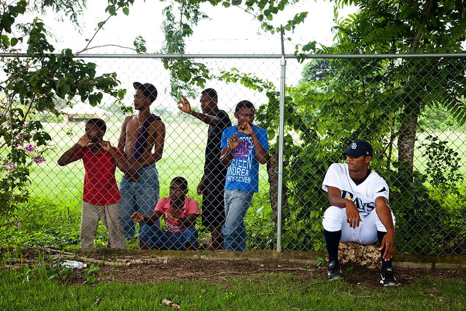 BOCA CHICA, DOMINICAN REPUBLIC. A professional player waits for foul balls near the fence line that separates the local kids. Most young boys dream of becoming a professional player where signing bonuses often exceed six figures.