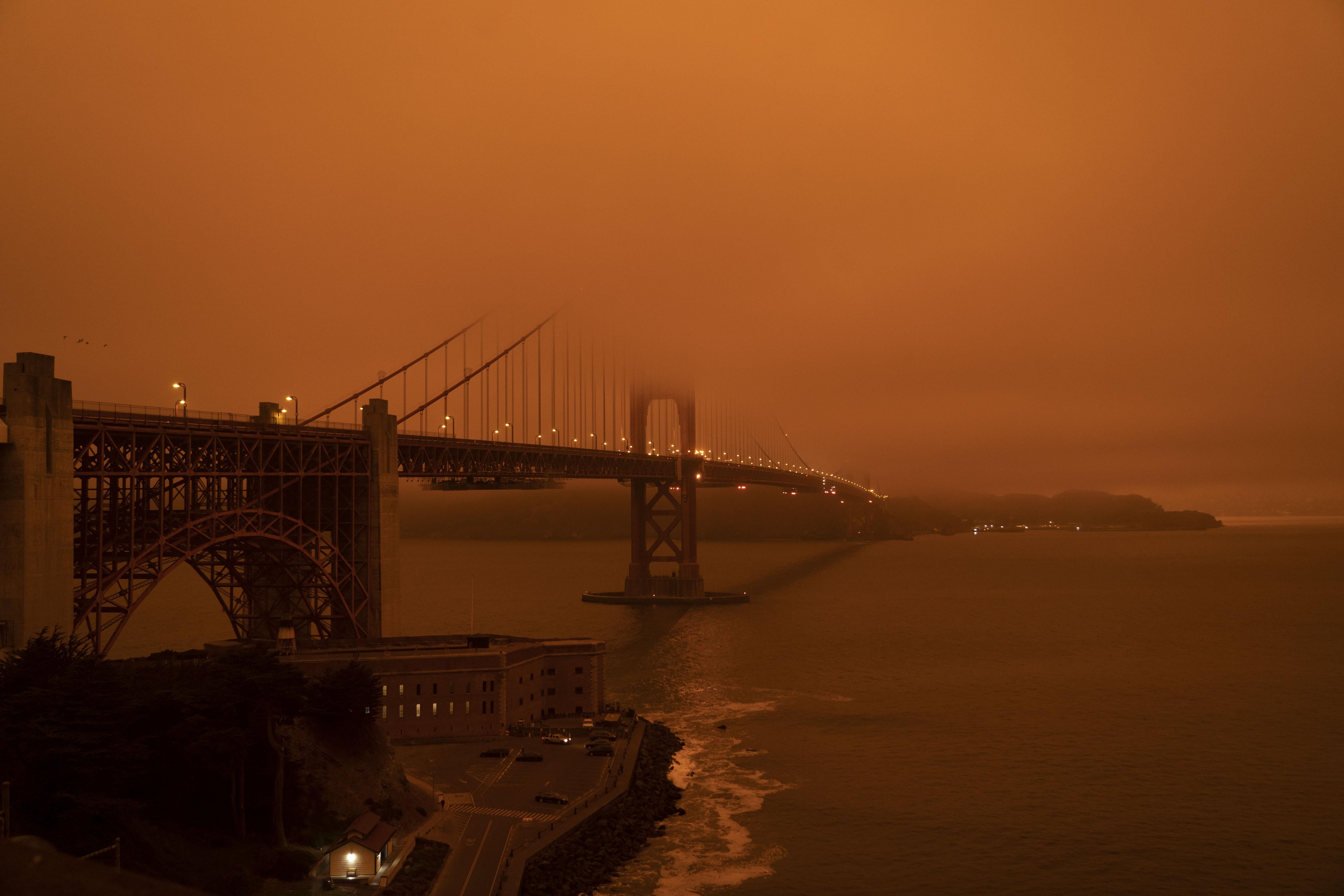Cars drive along the Golden Gate Bridge under an orange smoke filled sky at midday in San Francisco in September. 