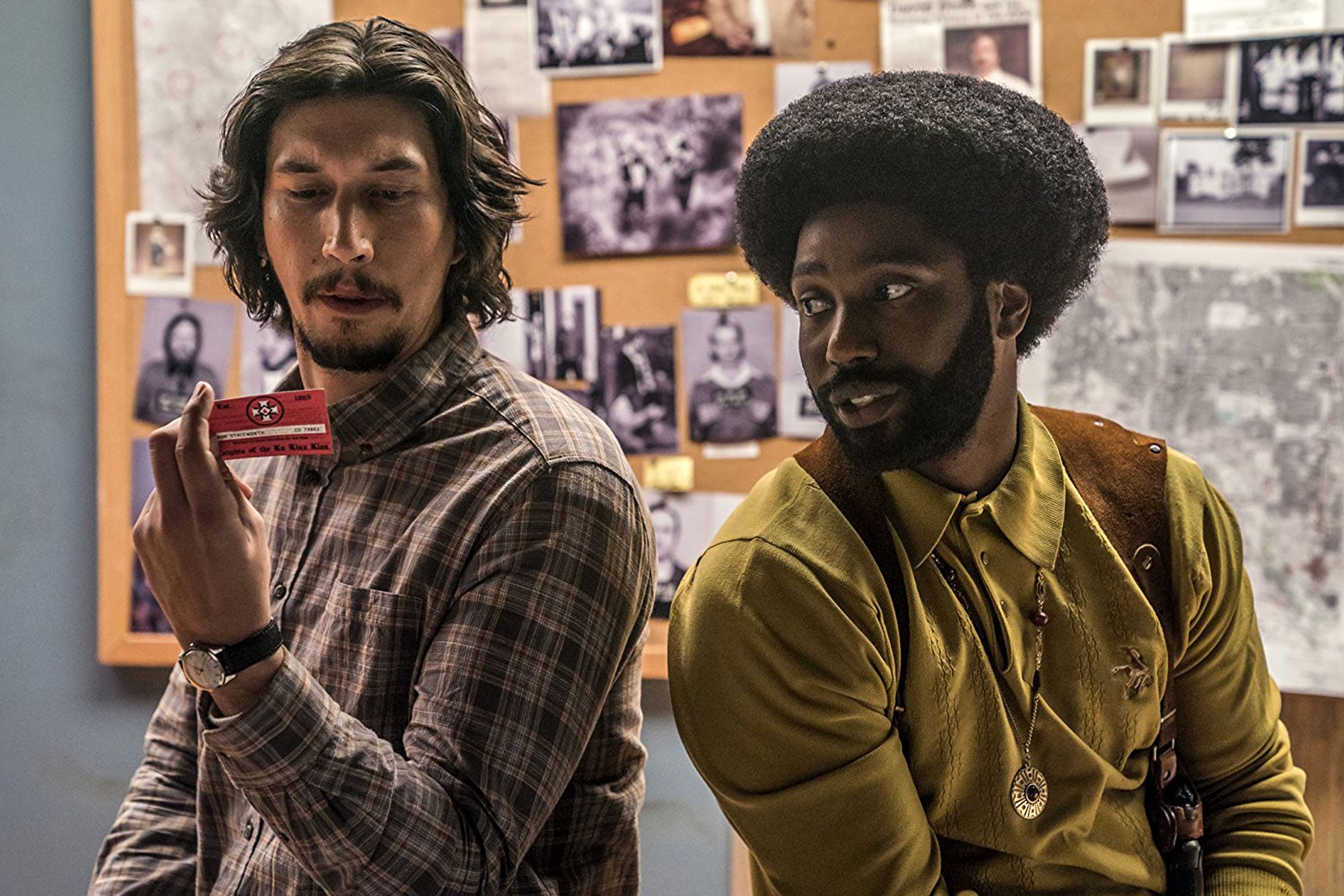 In a scene from BlacKkKlansman, Detective Flip Zimmerman (Adam Driver) holds a Ku Klux Klan membership card while Detective Ron Stallworth looks on.