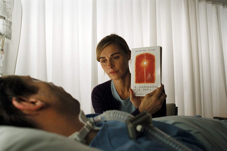 Mathieu Amalric and Anne Consigny in The Diving Bell and the Butterfly. He lies in a bed while she holds up a book with the title Le scaphandre et le papillon.