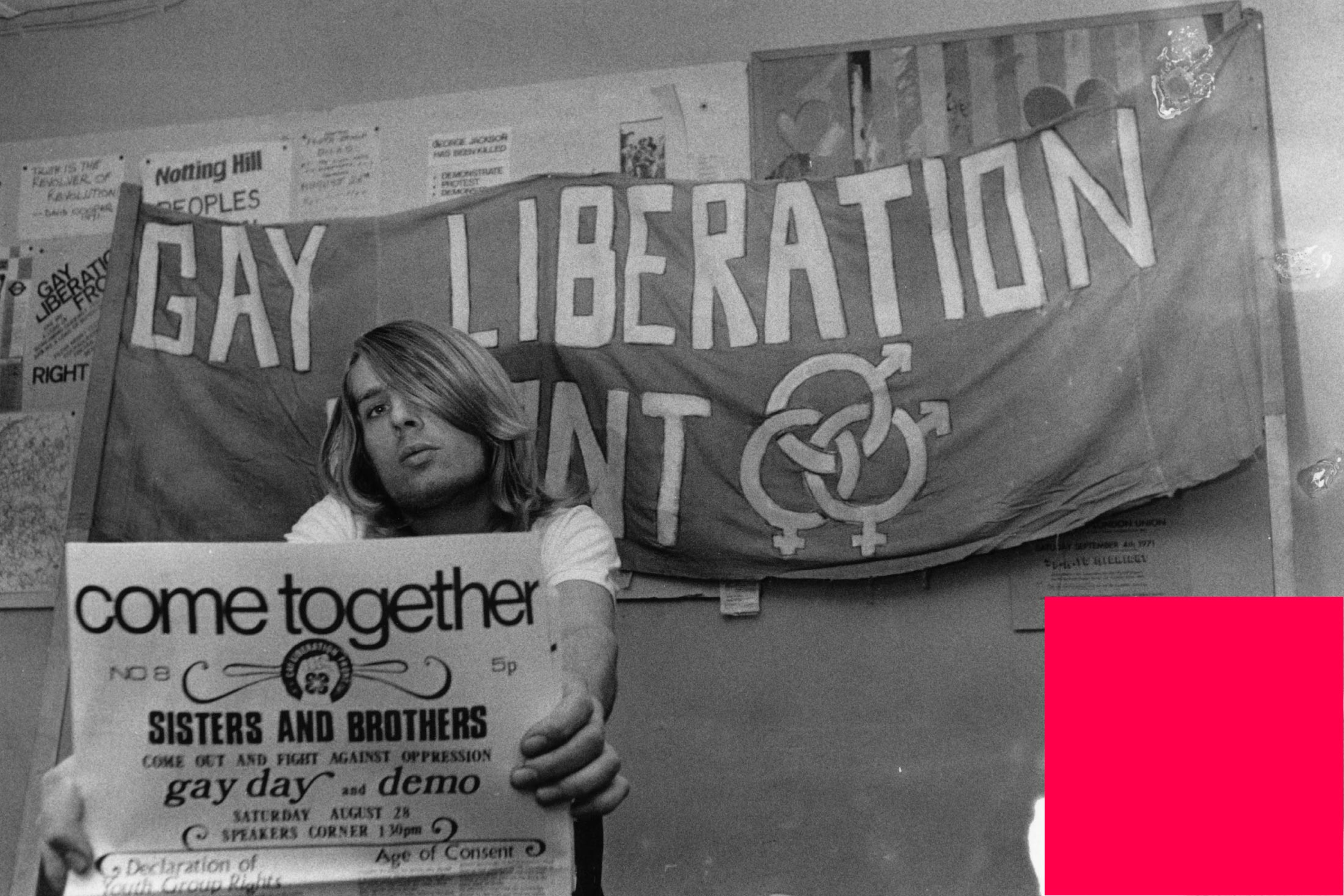 A member of the Gay Liberation Front holding a poster and under a banner. 