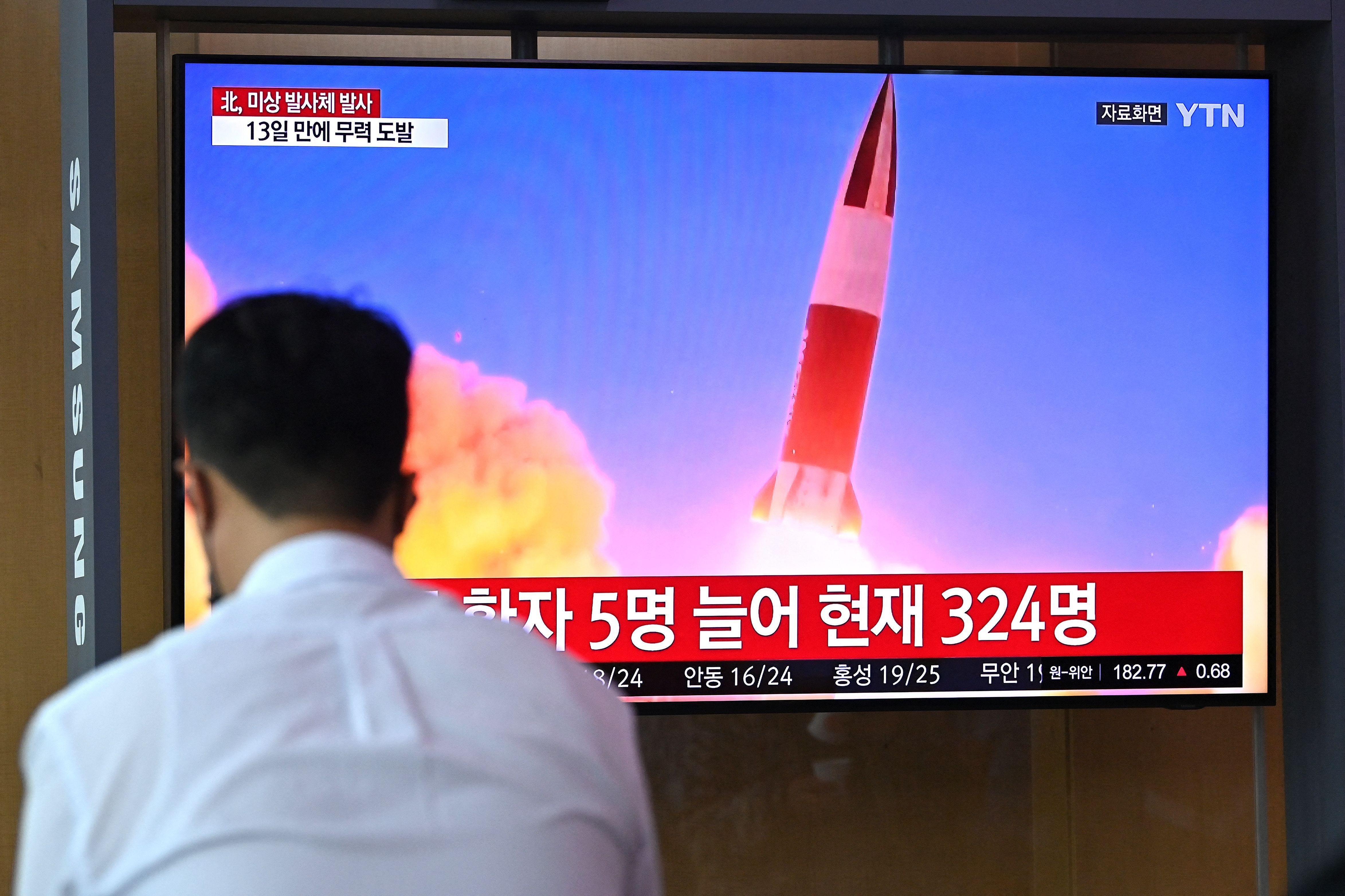 Back of a man's head in the foreground and a TV showing a missile launch in the background
